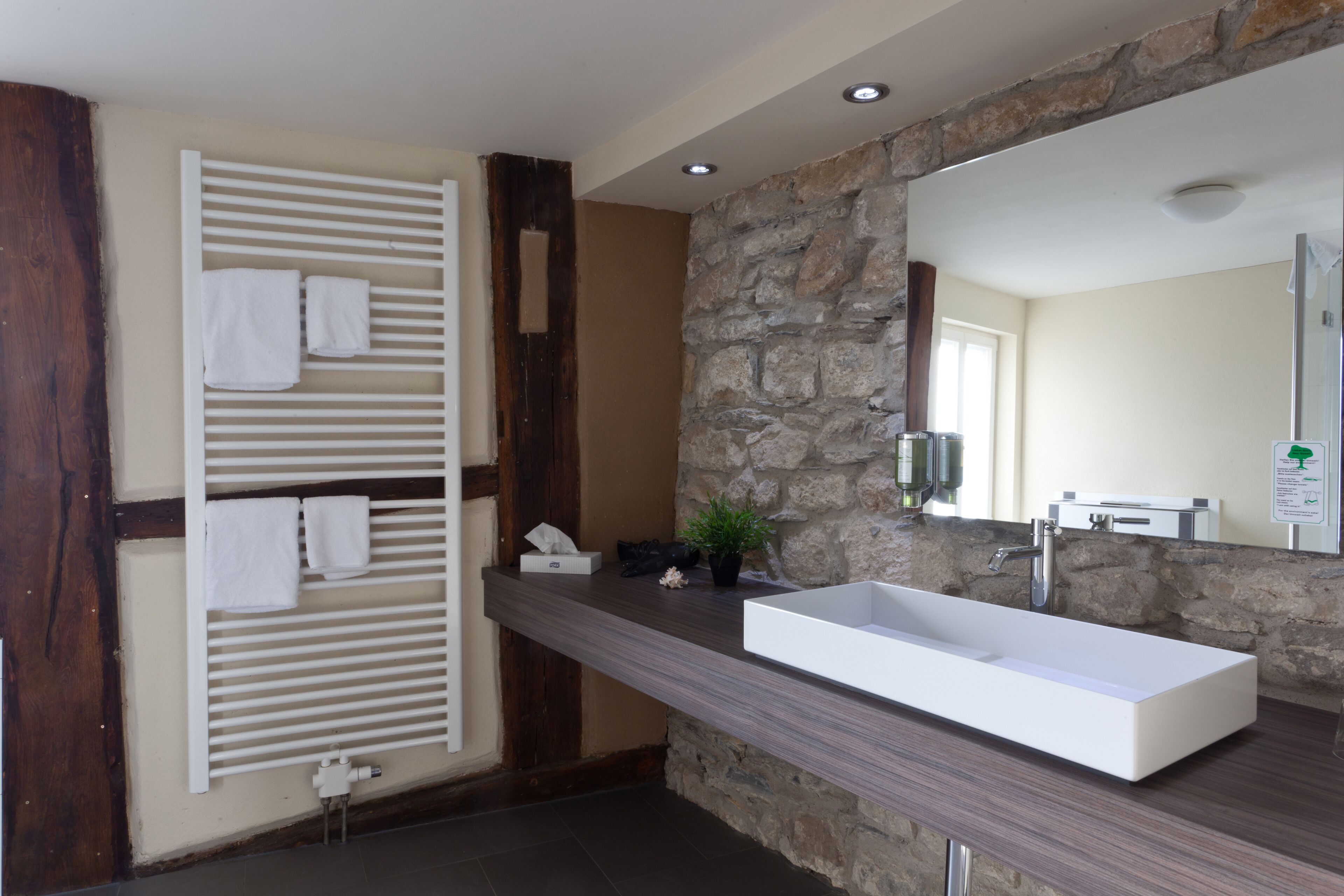 Een moderne badkamer met een accentmuur van steen, een groot rechthoekig wastafelmeubel en een handdoekrek met meerdere handdoeken.