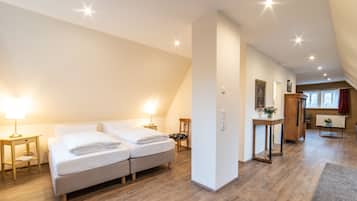 A hotel room with a double bed, a bedside table with a lamp, a wooden floor, and a view of the hallway.