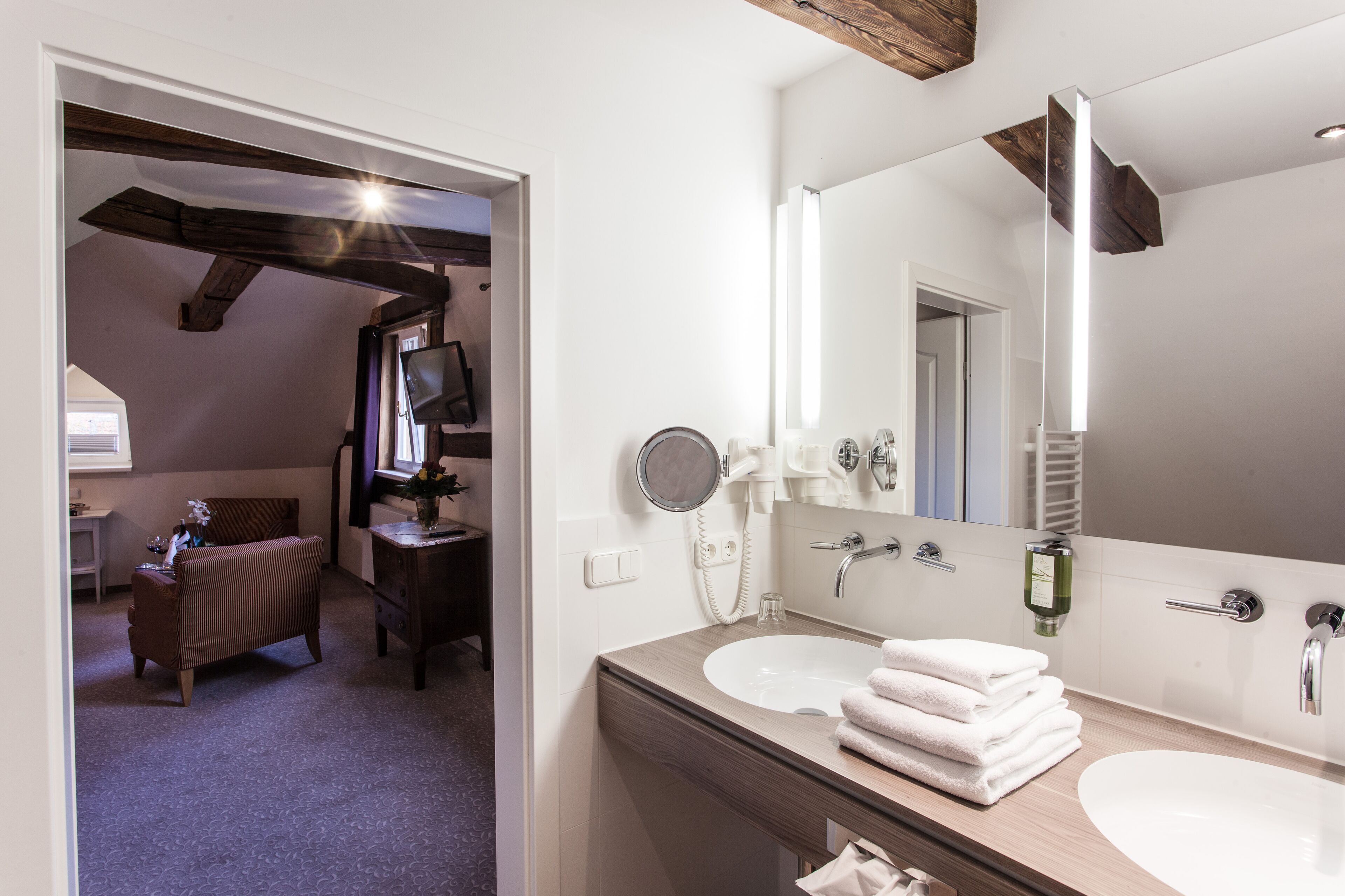 A bathroom with a wooden vanity, two sinks, a large mirror, and a towel stack.