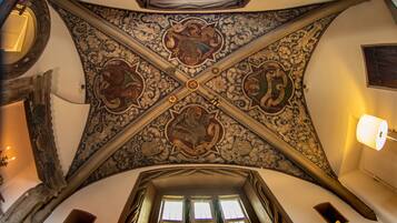 Une pièce aux hauts plafonds, ornée de motifs complexes, avec une grande fenêtre dotée de rideaux et une lampe fixée au mur.