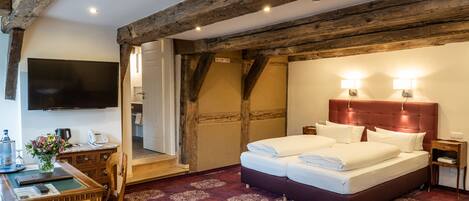 A hotel room with a large bed, wooden beams, a flat-screen TV, a desk with a chair, and a red carpet.