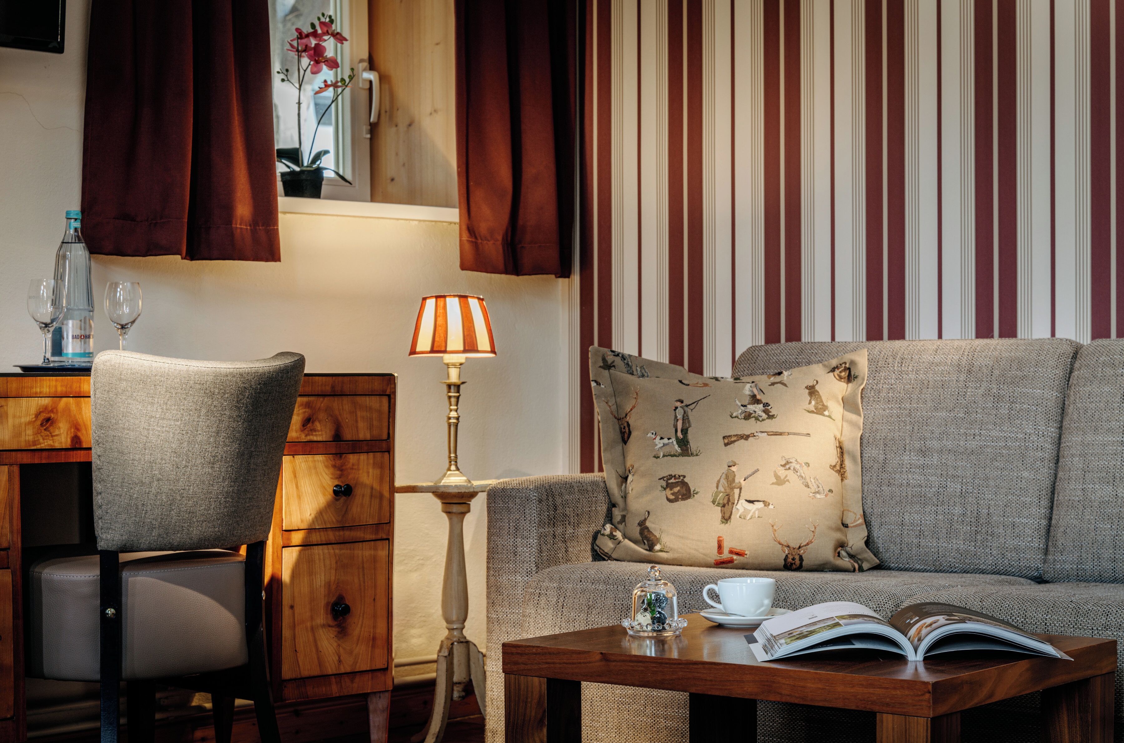 Ein gemütliches Wohnzimmer mit einer Couch, einem Sessel, einem Holztisch und einer Lampe.