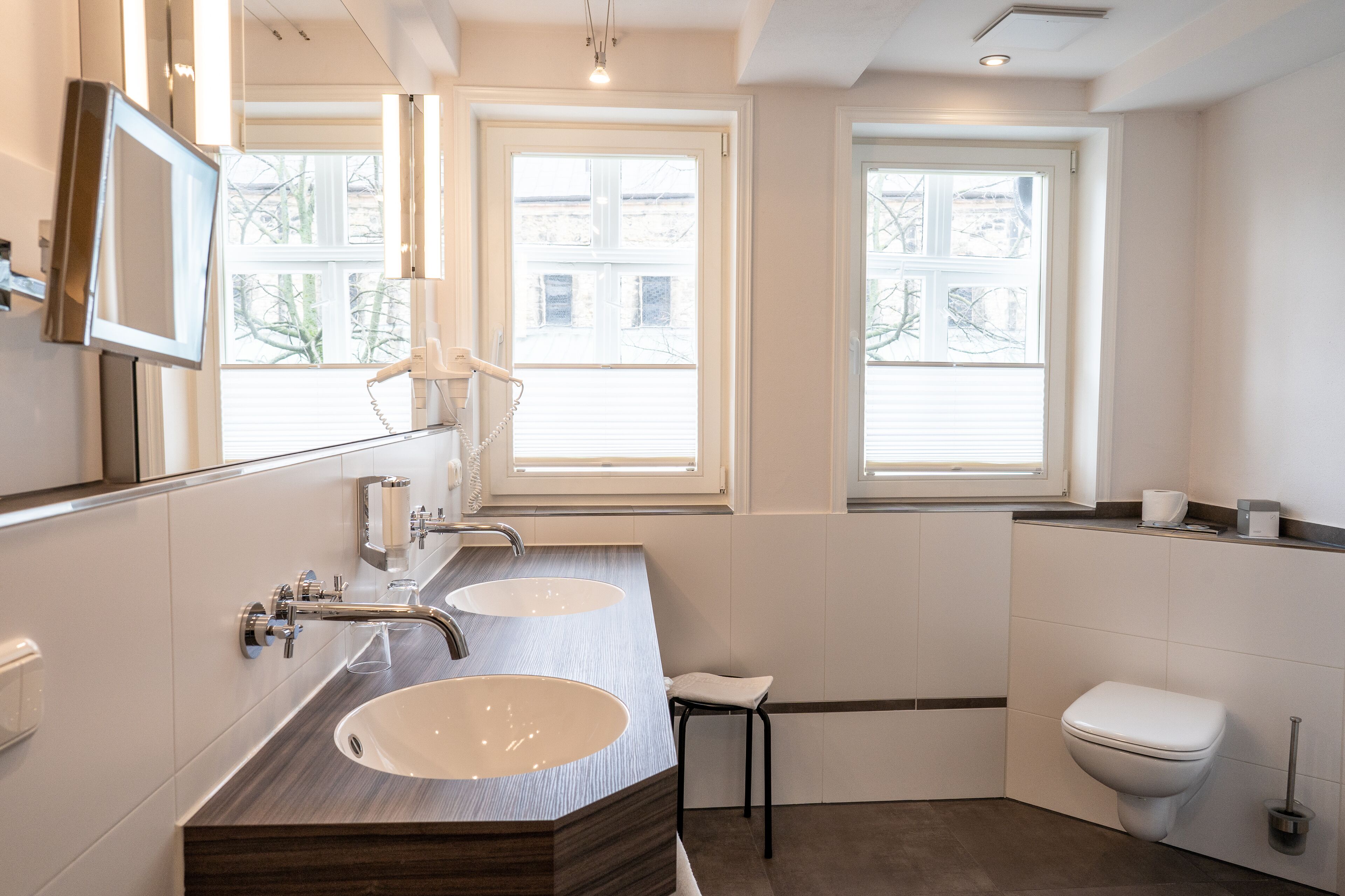 Ein modernes Badezimmer mit zwei Waschbecken, einer Toilette und einem Fenster.