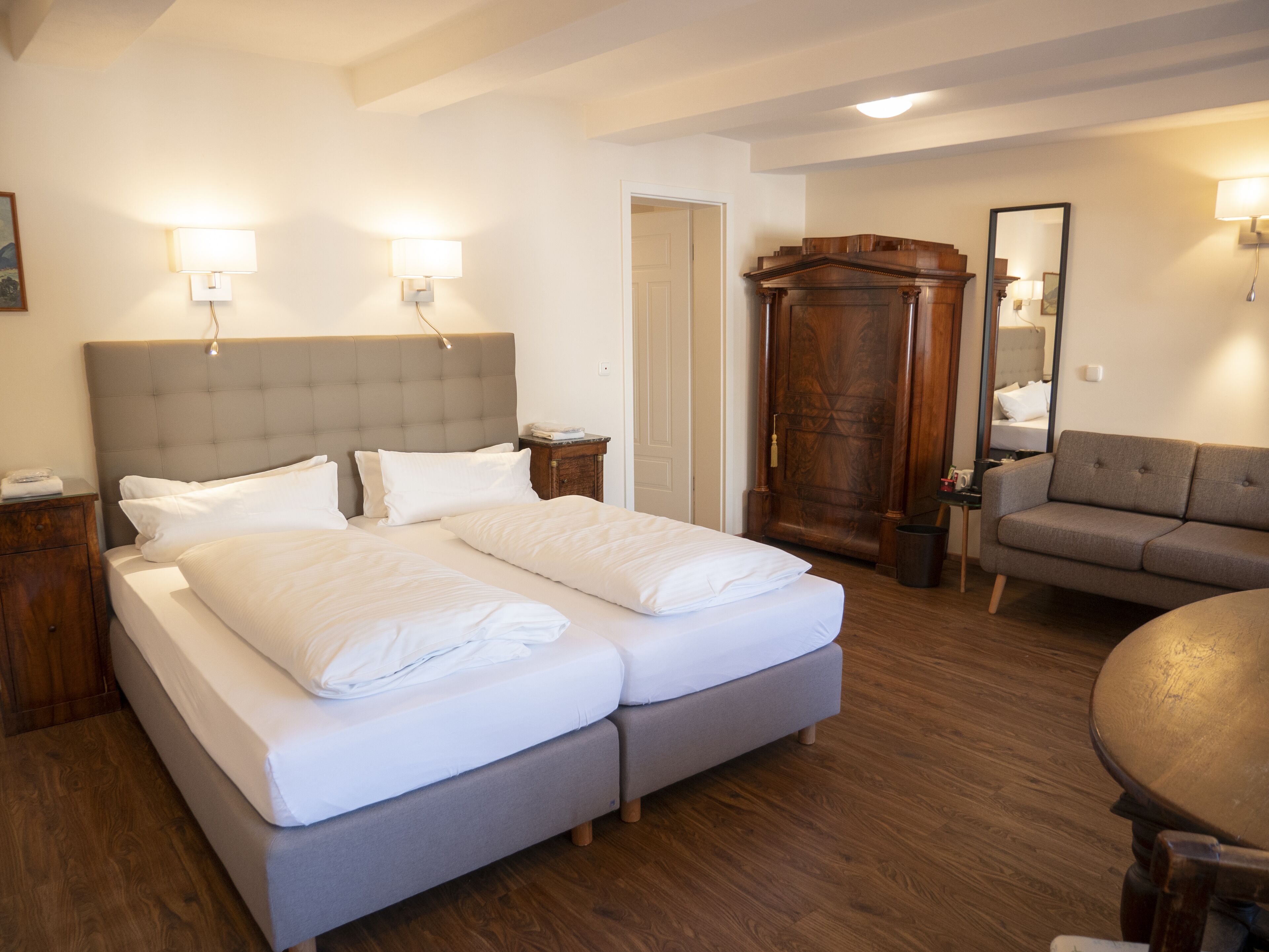A hotel room with a large bed, bedside tables, a wardrobe, a sofa, and a mirror.