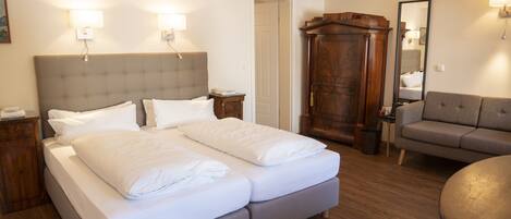 A hotel room with a large bed, bedside tables, a wardrobe, a sofa, and a mirror.