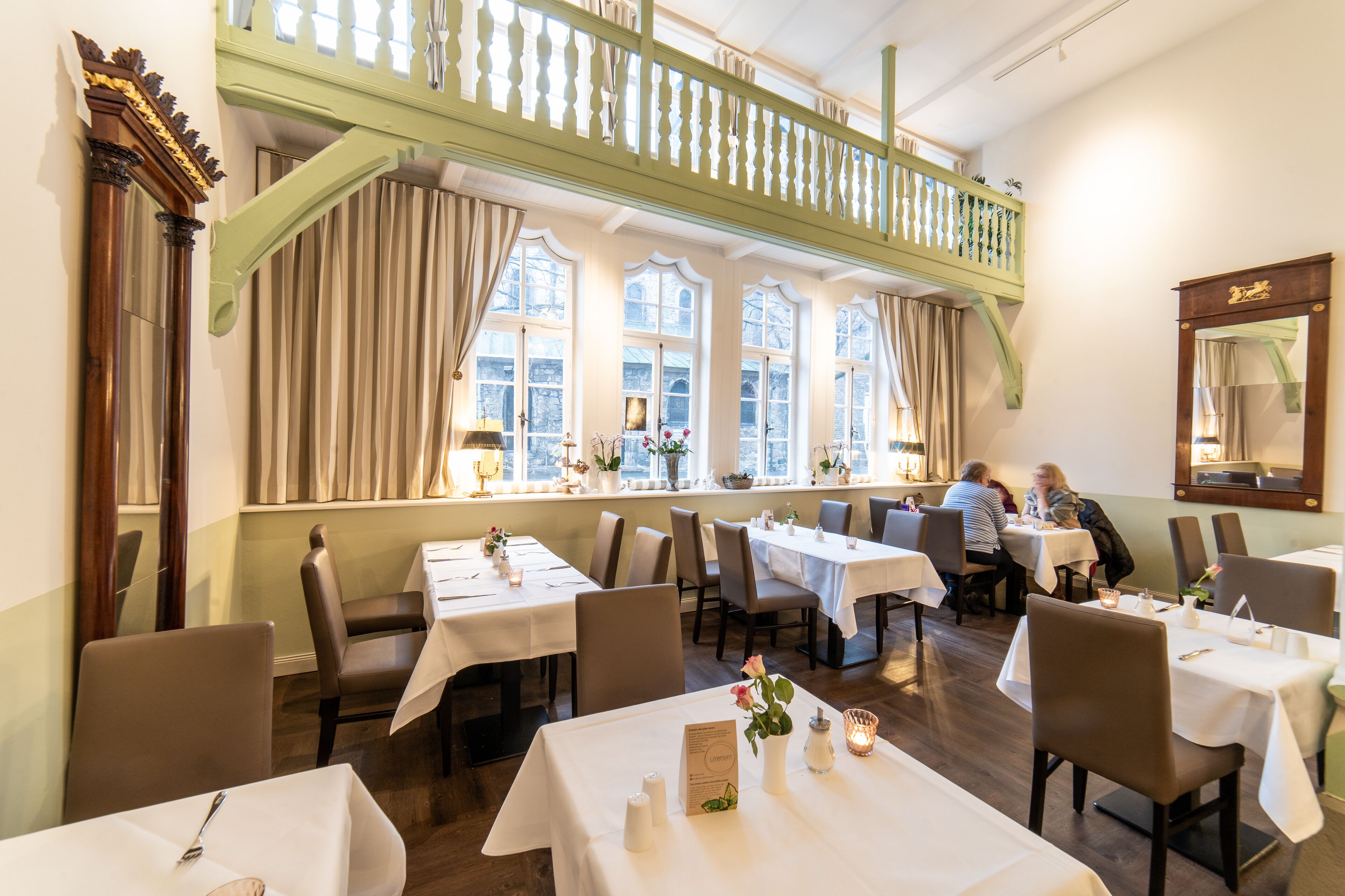 A restaurant with multiple tables, chairs, and a balcony with a railing.