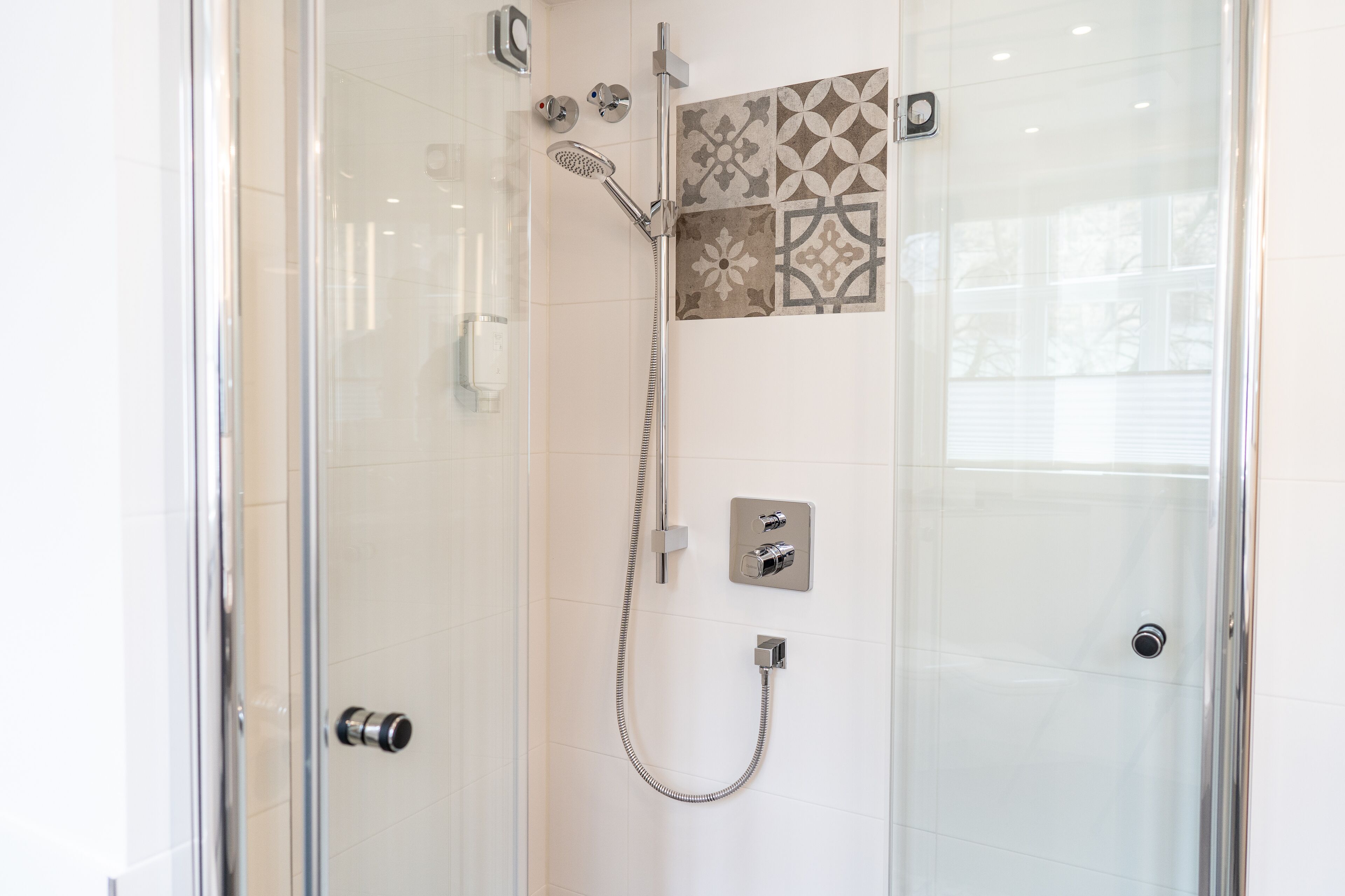 A glass-enclosed shower with a handheld showerhead and a wall-mounted control panel.