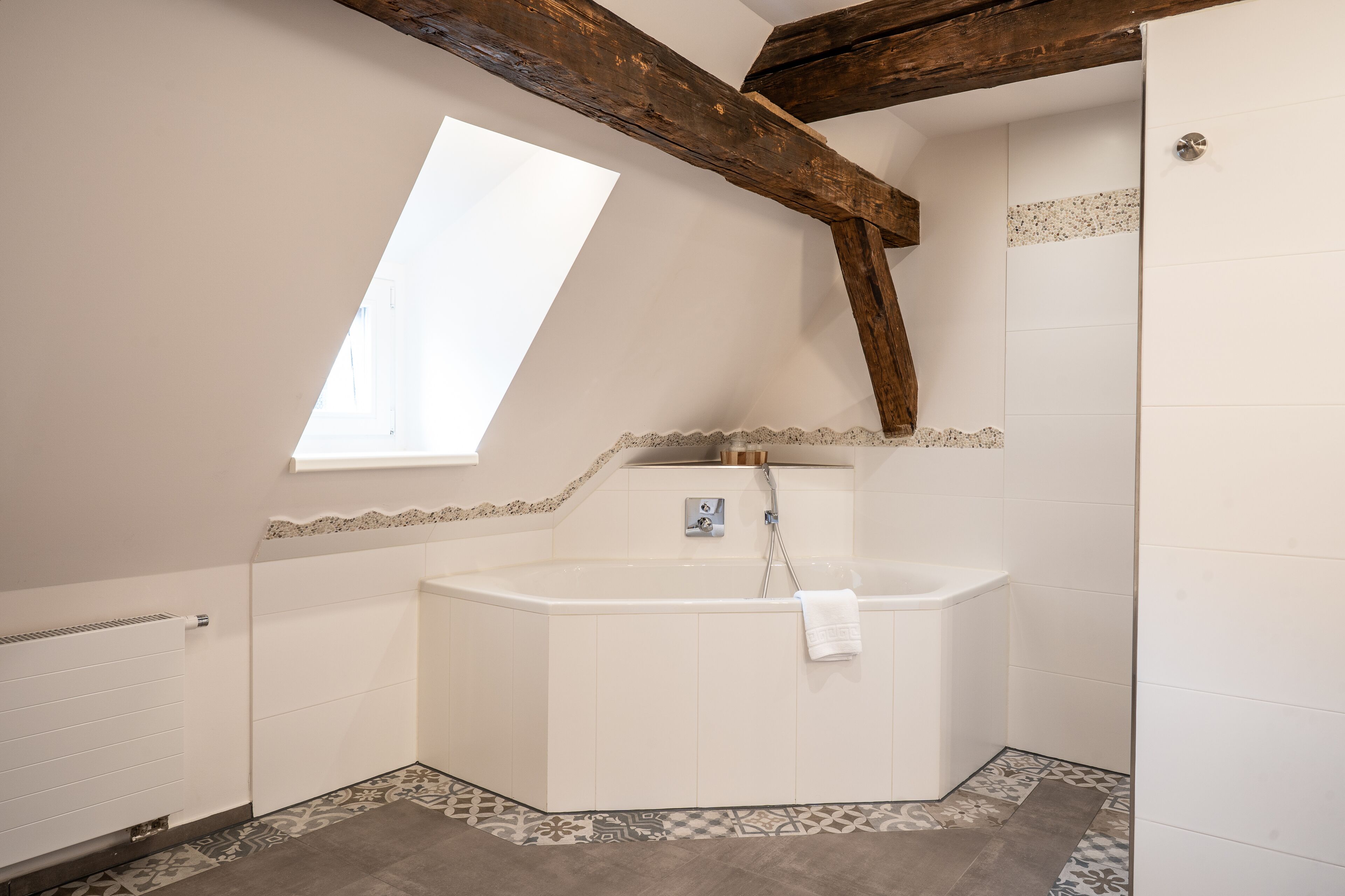 Ein Badezimmer mit einer freistehenden Badewanne, einem Fenster und einer schrägen Decke mit freiliegenden Holzbalken.