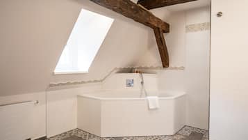 Ein Badezimmer mit einer freistehenden Badewanne, einem Fenster und einer schrägen Decke mit freiliegenden Holzbalken.