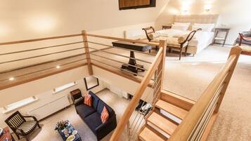 Ein geräumiges Schlafzimmer im Loft-Stil mit einem großen Bett, einer Sitzecke mit einer Couch und Sesseln sowie einer Holztreppe.