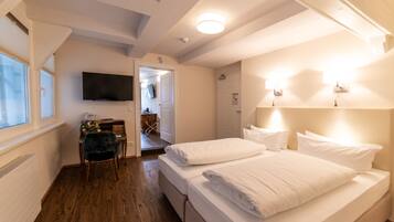 A hotel room with a bed, a desk, a chair, and a television on the wall.