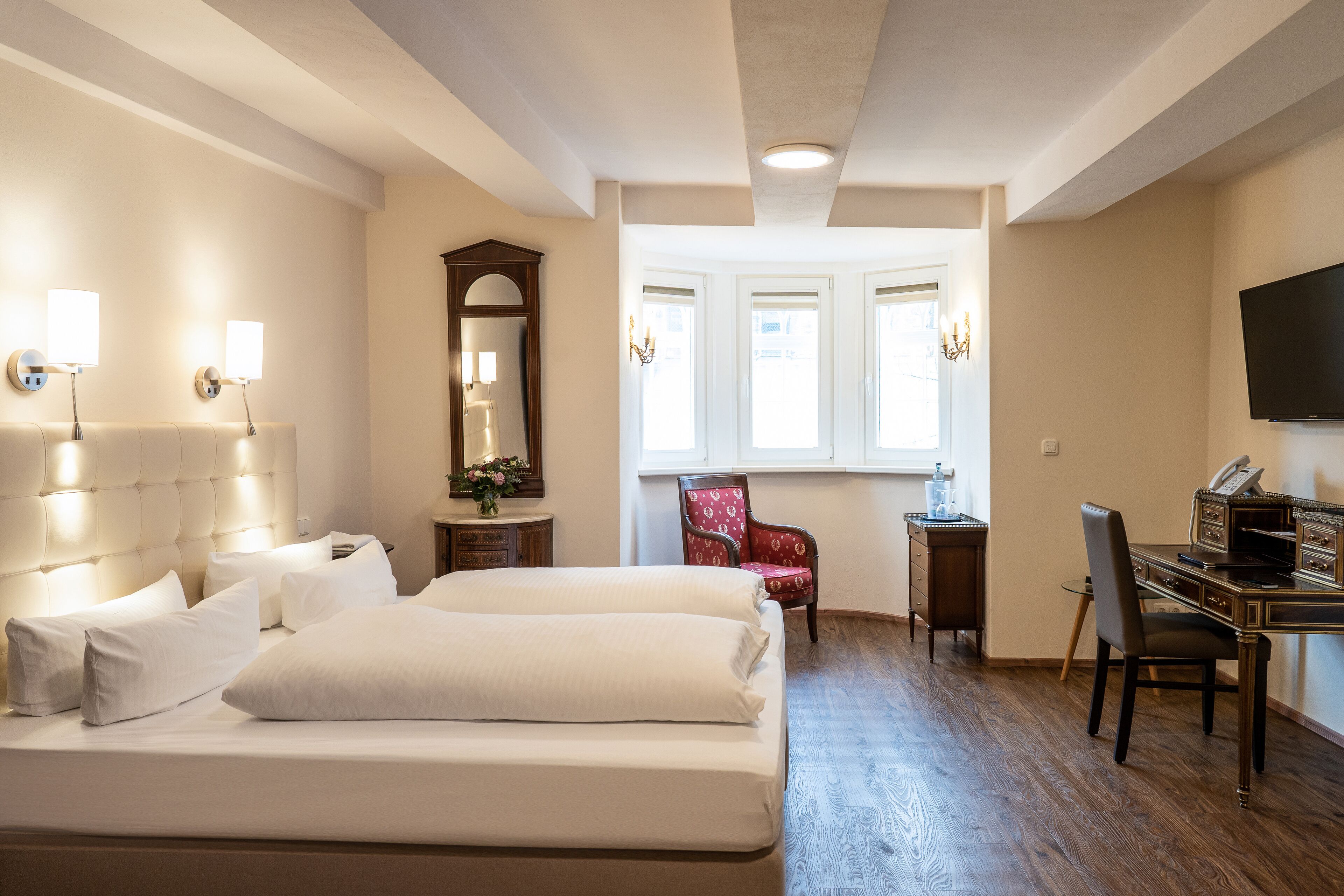 A hotel room with a large bed, a desk, a chair, a TV, and a window with a view.