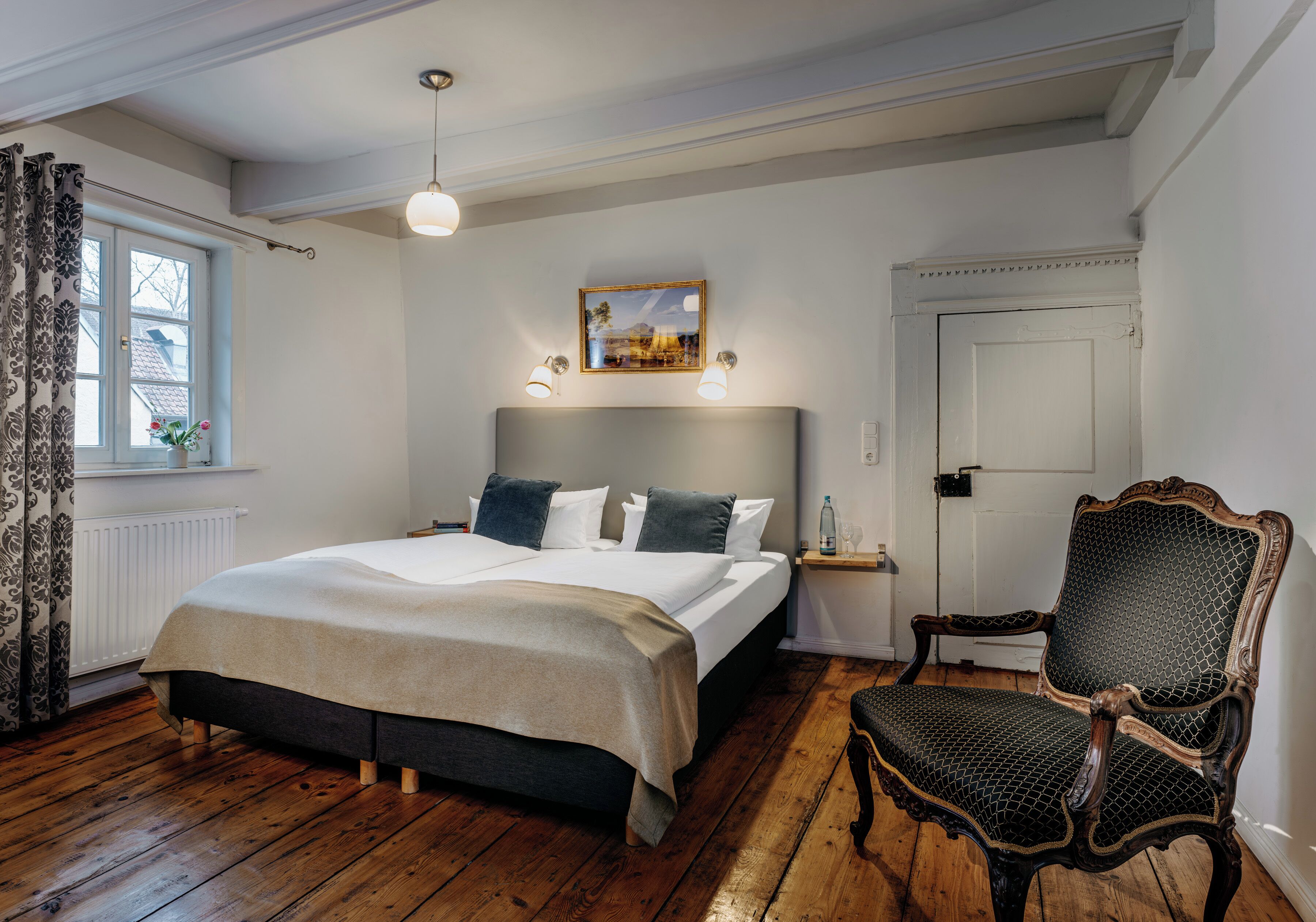 A bedroom with a large bed, a chair, a nightstand, and a window with curtains.