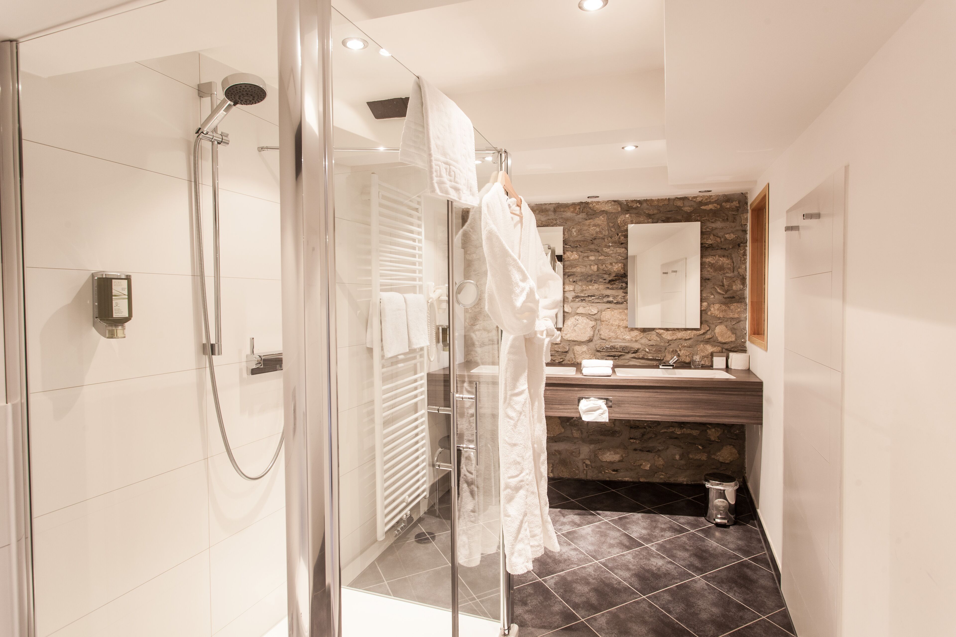 A modern bathroom with a glass-enclosed shower, a wooden vanity, and a stone accent wall.