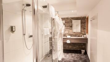 A modern bathroom with a glass-enclosed shower, a wooden vanity, and a stone accent wall.