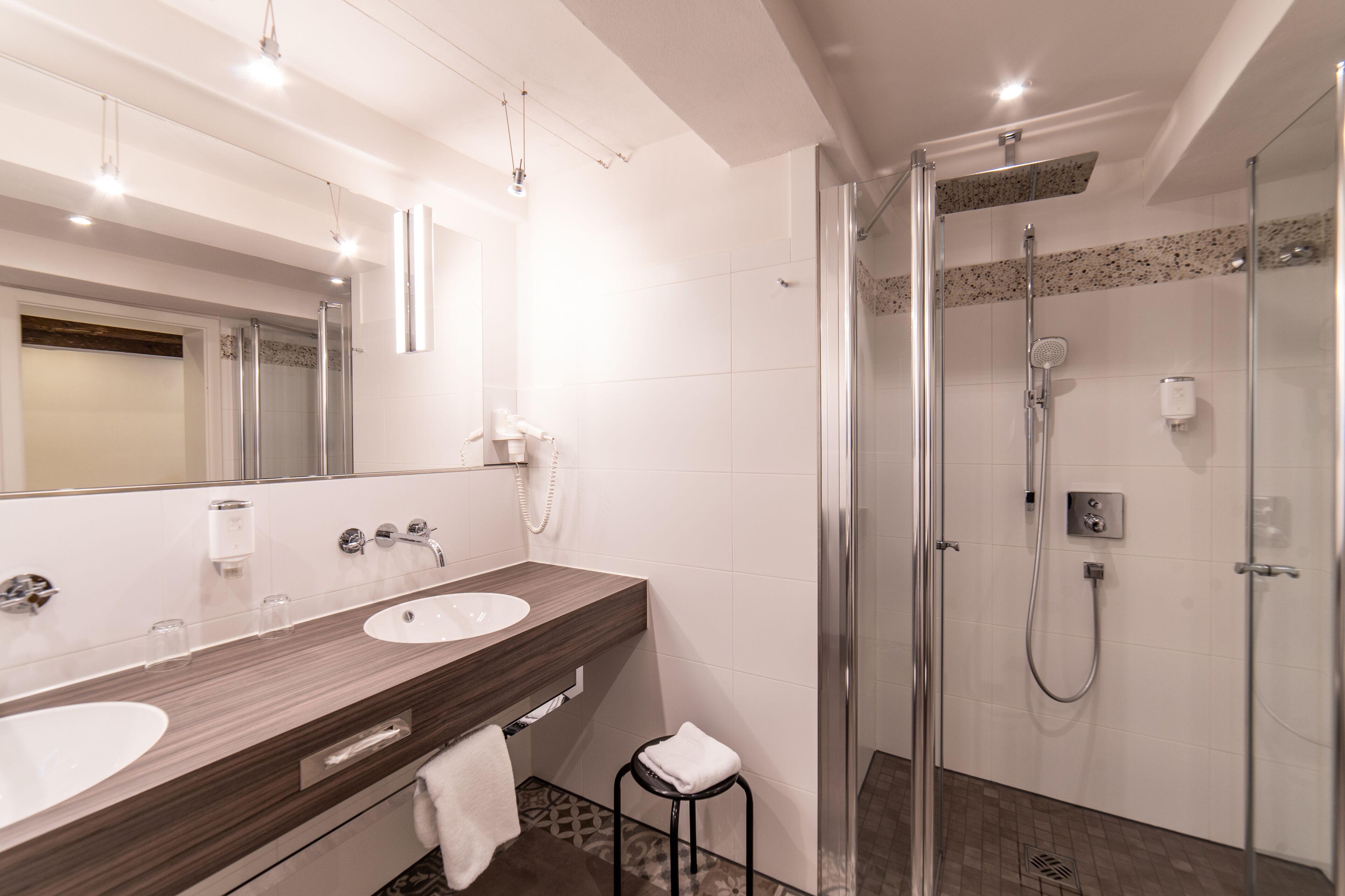 Un baño moderno con dos lavamanos, ducha con mampara de vidrio y un espejo grande.