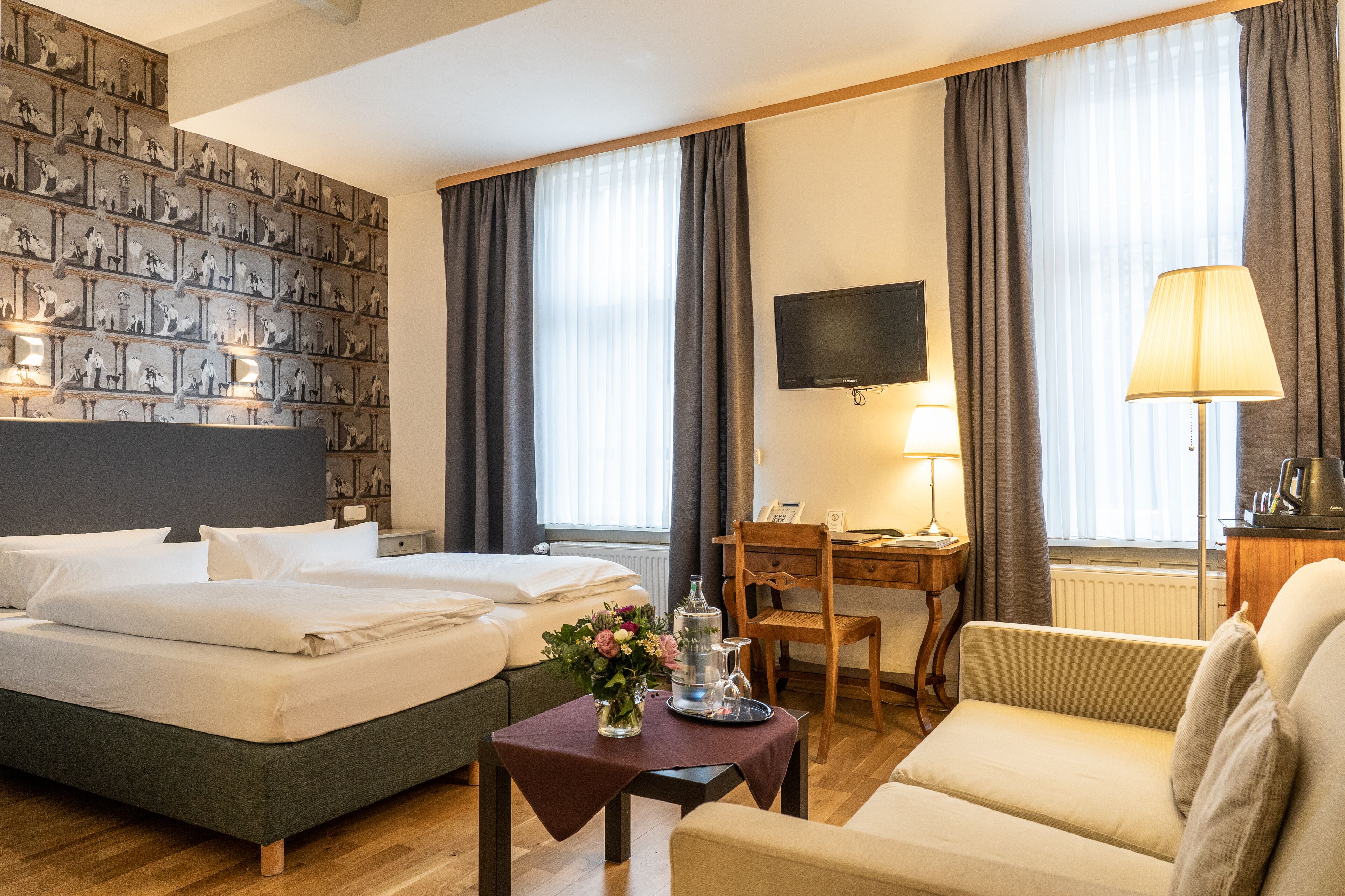Ein Hotelzimmer mit einem großen Bett, einem Schreibtisch, einem Sessel, einem Fernseher und einem Fenster mit Vorhängen.