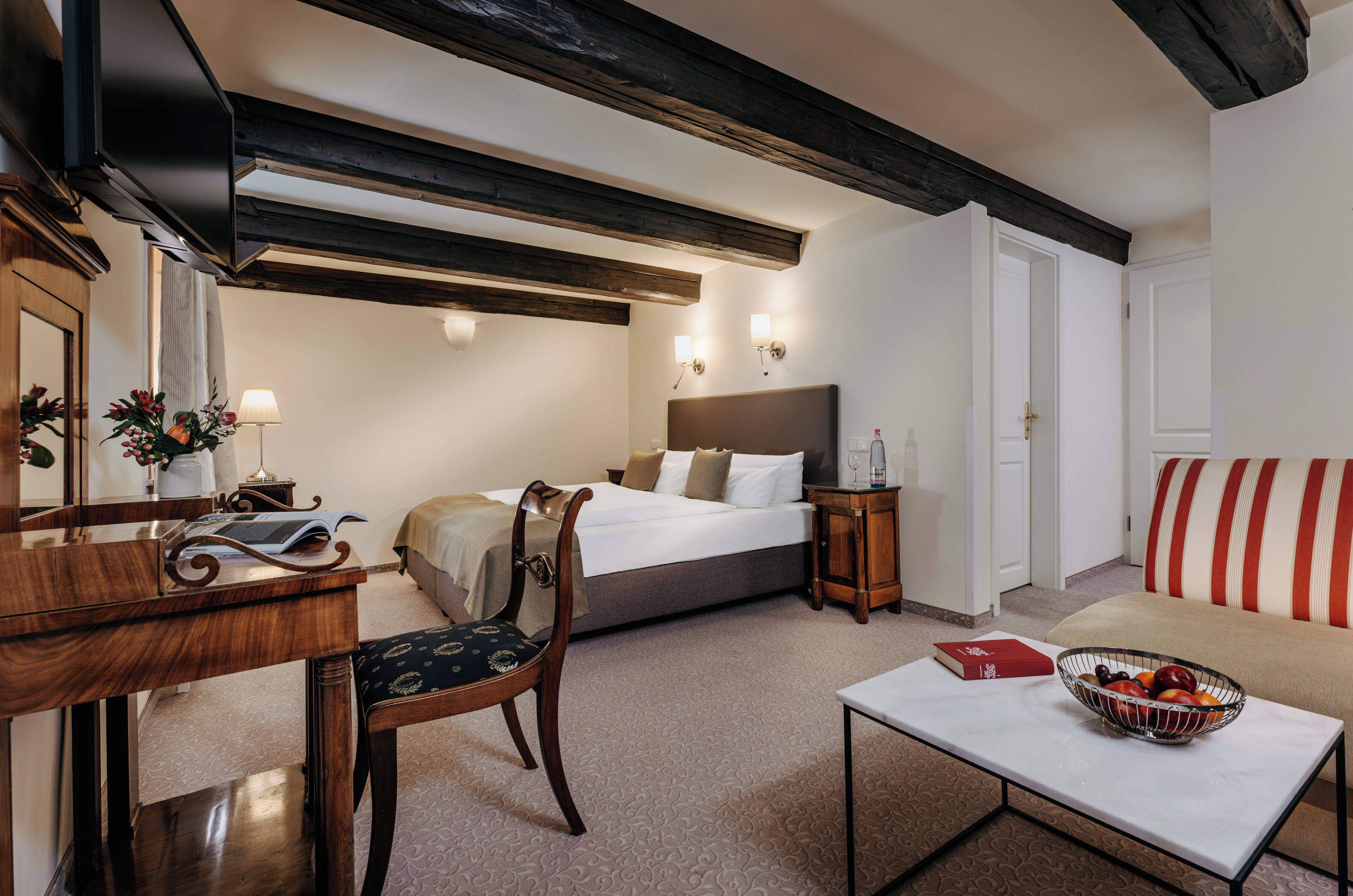 Une chambre d’hôtel comprenant un lit, un bureau, une chaise, une table avec un panier de fruits et un canapé.