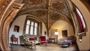 An arched room with intricate ceiling artwork, a red chair, a wooden table, and a sofa. - Romantik Hotel Alte Münze (Goslar)