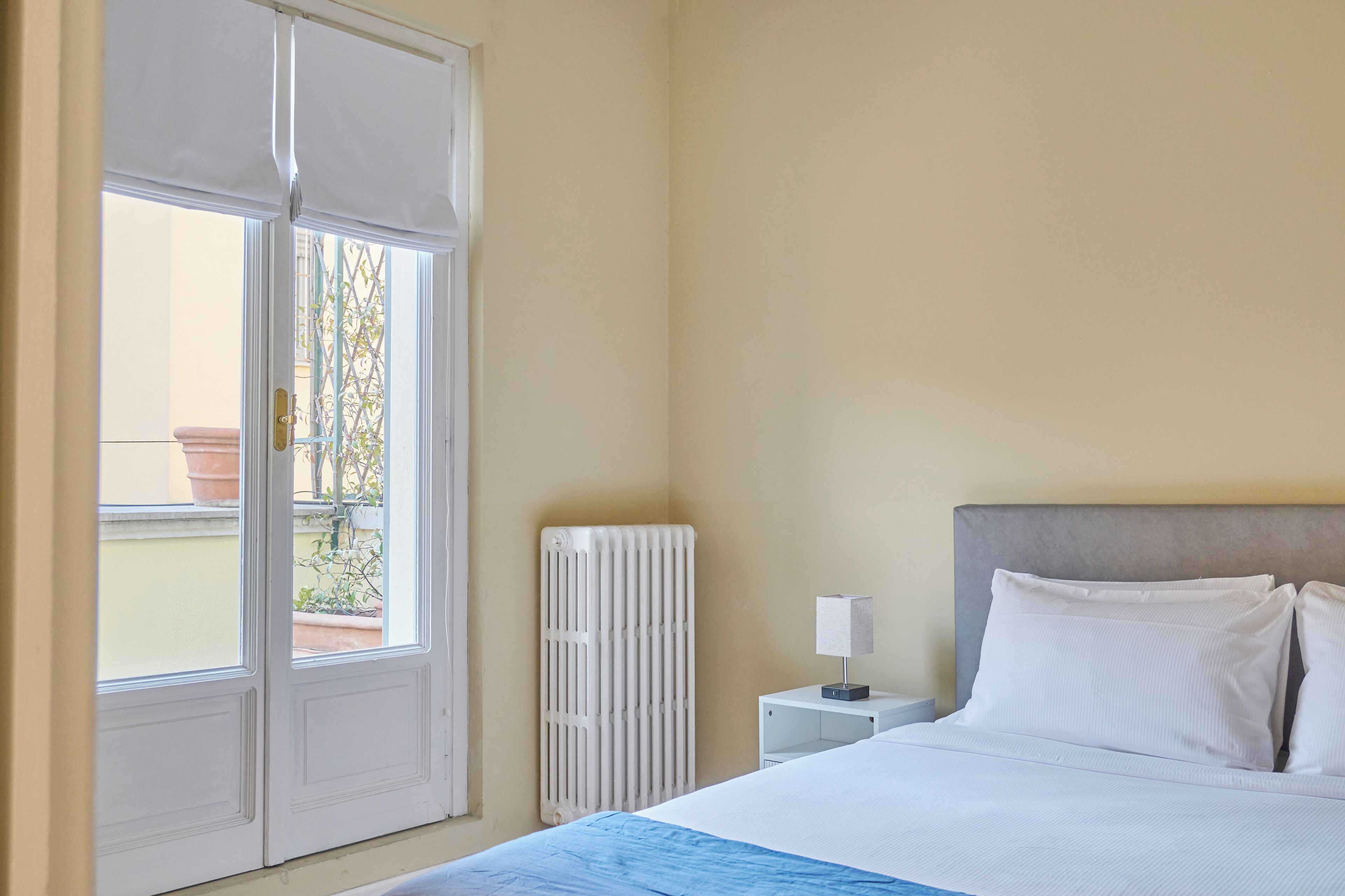 Ein Schlafzimmer mit einem Bett, einem Nachttisch, einem Heizkörper und einem Fenster mit Blick ins Freie.