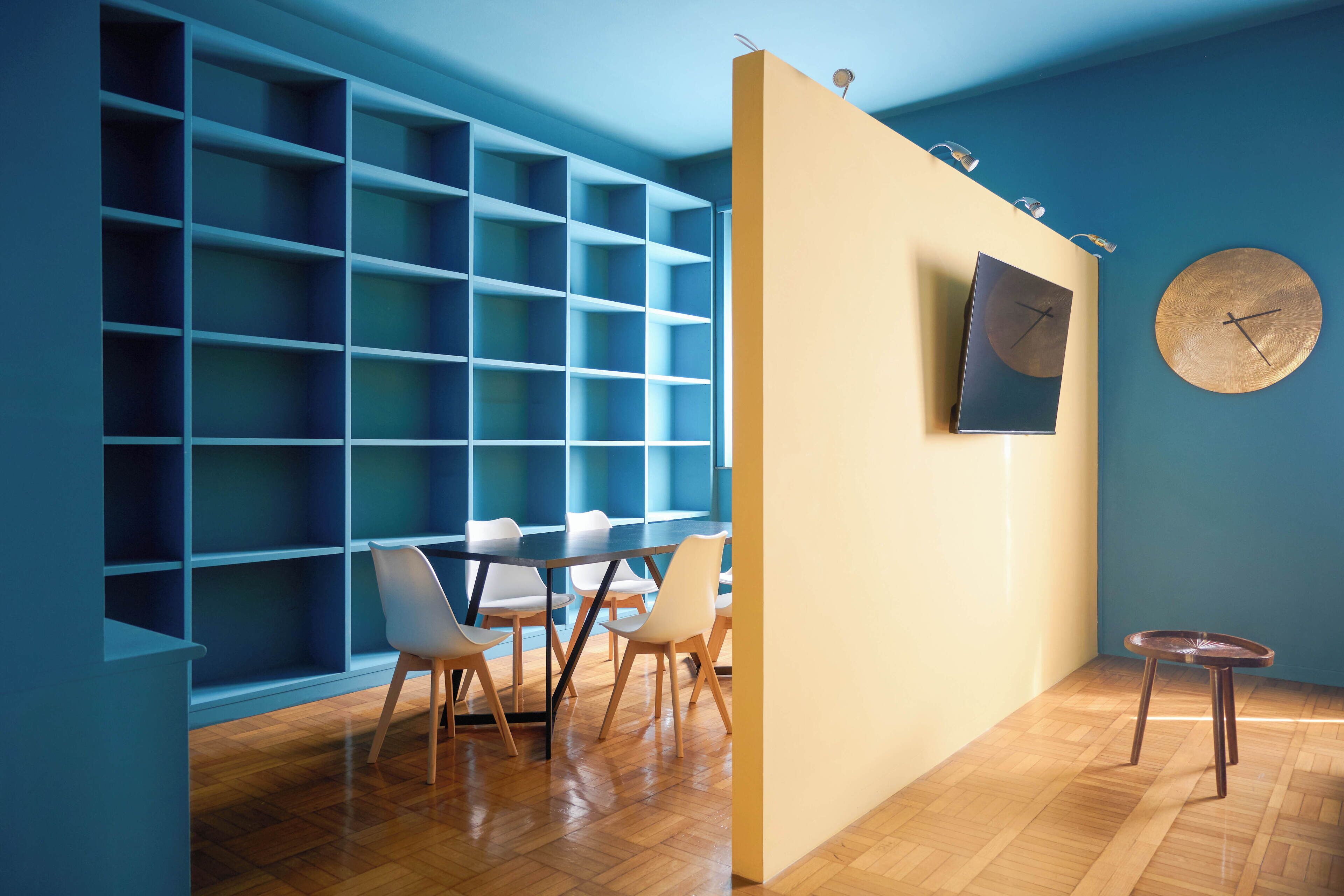 Une pièce moderne avec un plancher en bois, une table à manger avec des chaises, une bibliothèque, une horloge murale ronde et une petite table ronde.