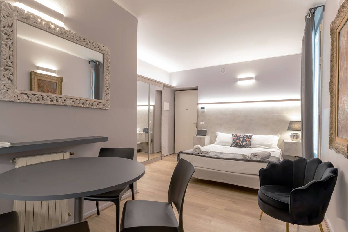 A modern hotel room with a large bed, a round dining table, and a black chair.