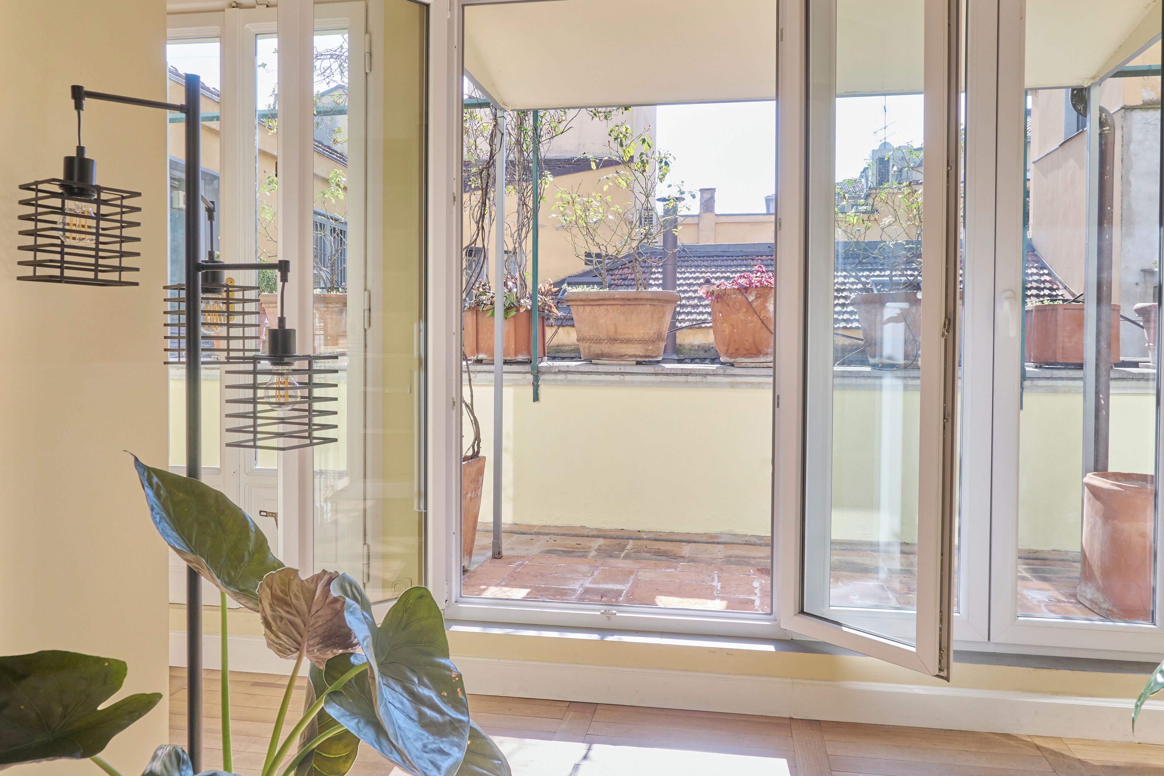A room with a sliding glass door leading to a balcony with potted plants and a tiled roof.