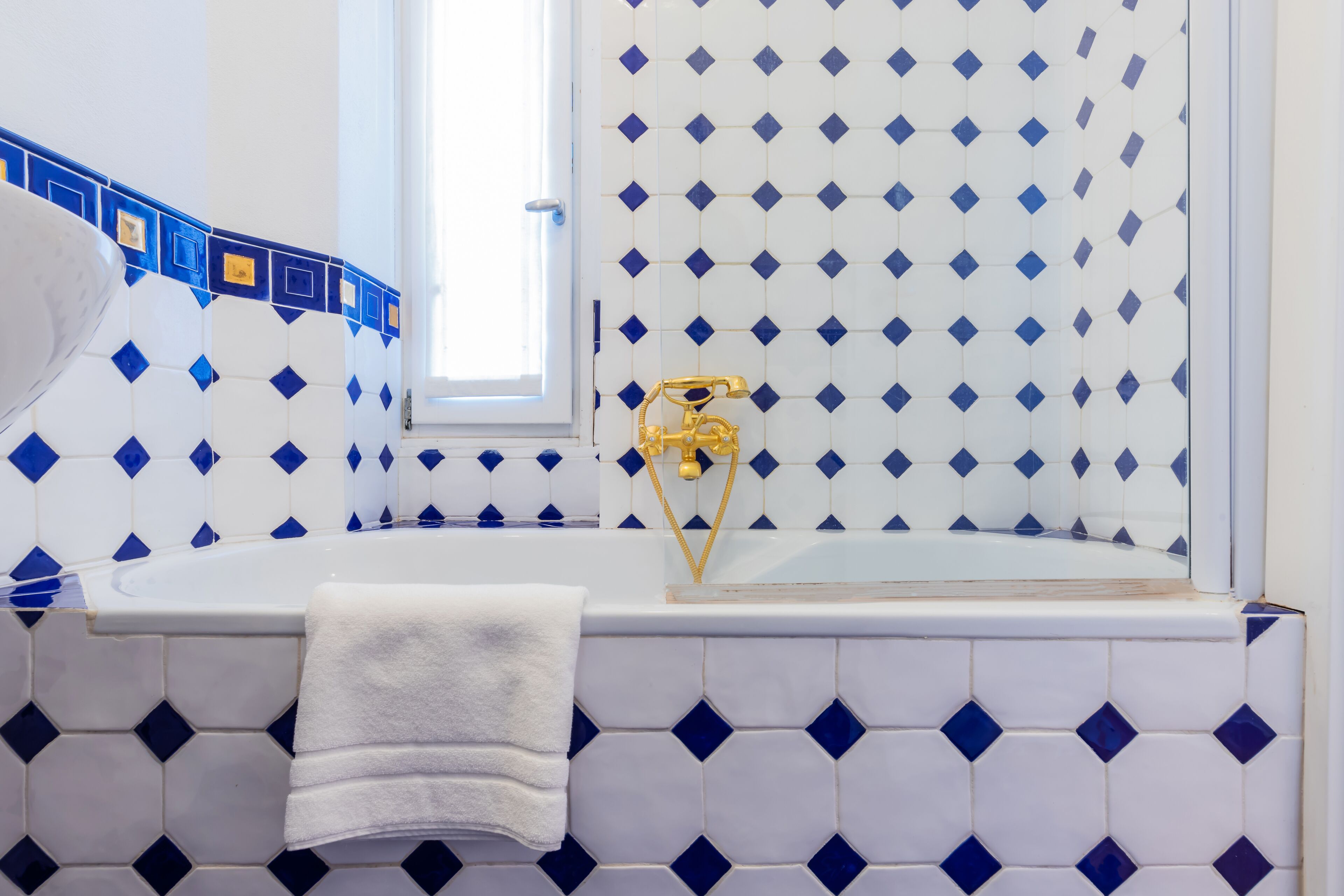 A bathroom with a white bathtub, a gold faucet, and a blue and white tiled wall.