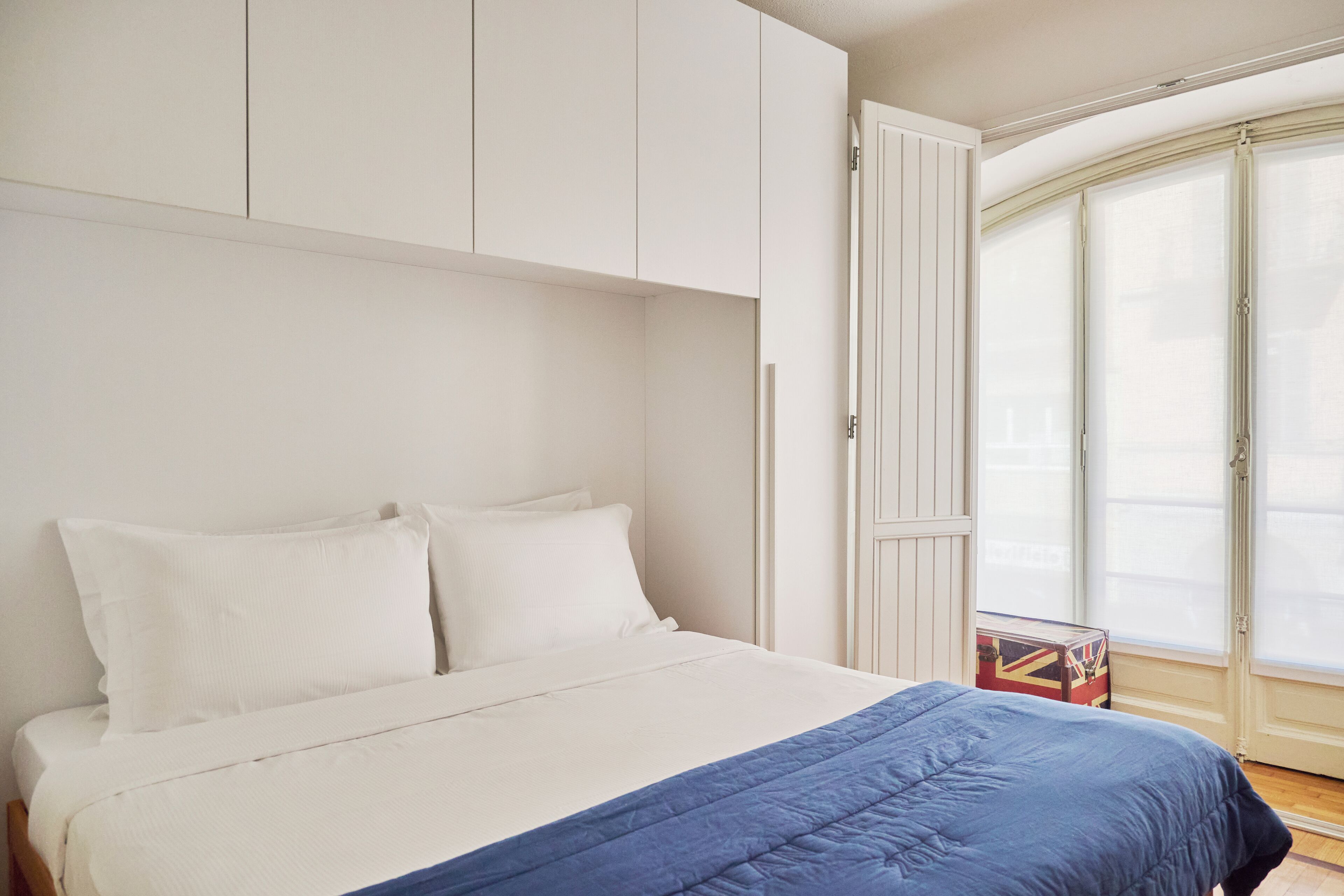 Une chambre à coucher avec un lit, des murs blancs, une fenêtre et une porte.
