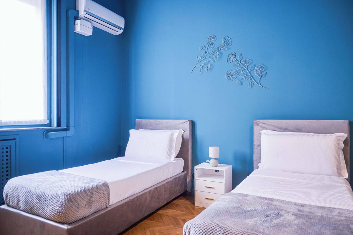 A room with two beds, a window with an air conditioner, and a wall decoration.