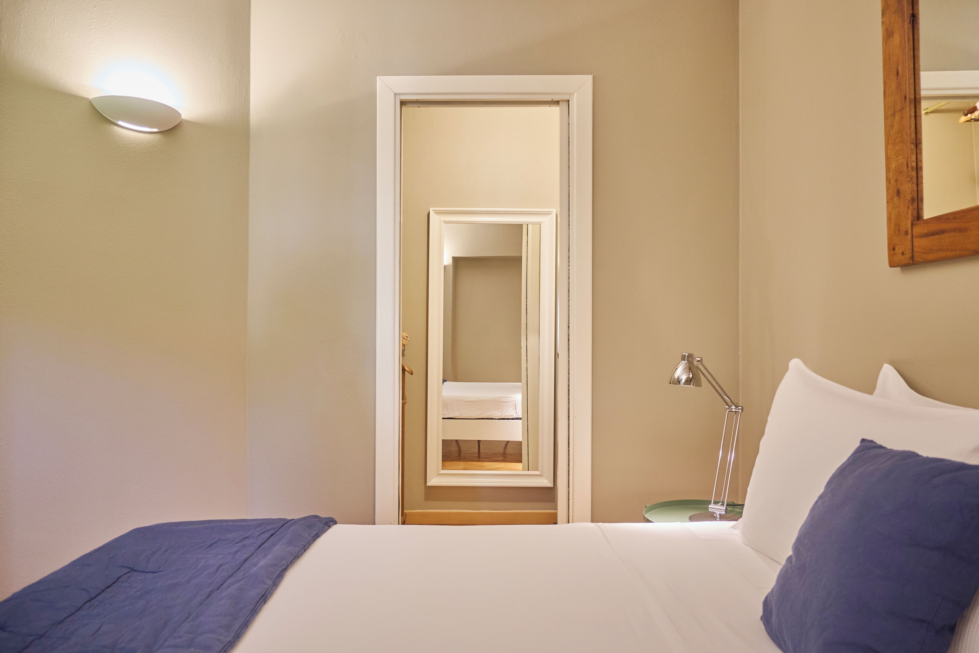 Ein Hotelzimmer mit einem Bett, einem Nachttisch, einer Lampe, einem Spiegel und einer Tür zu einem Badezimmer.