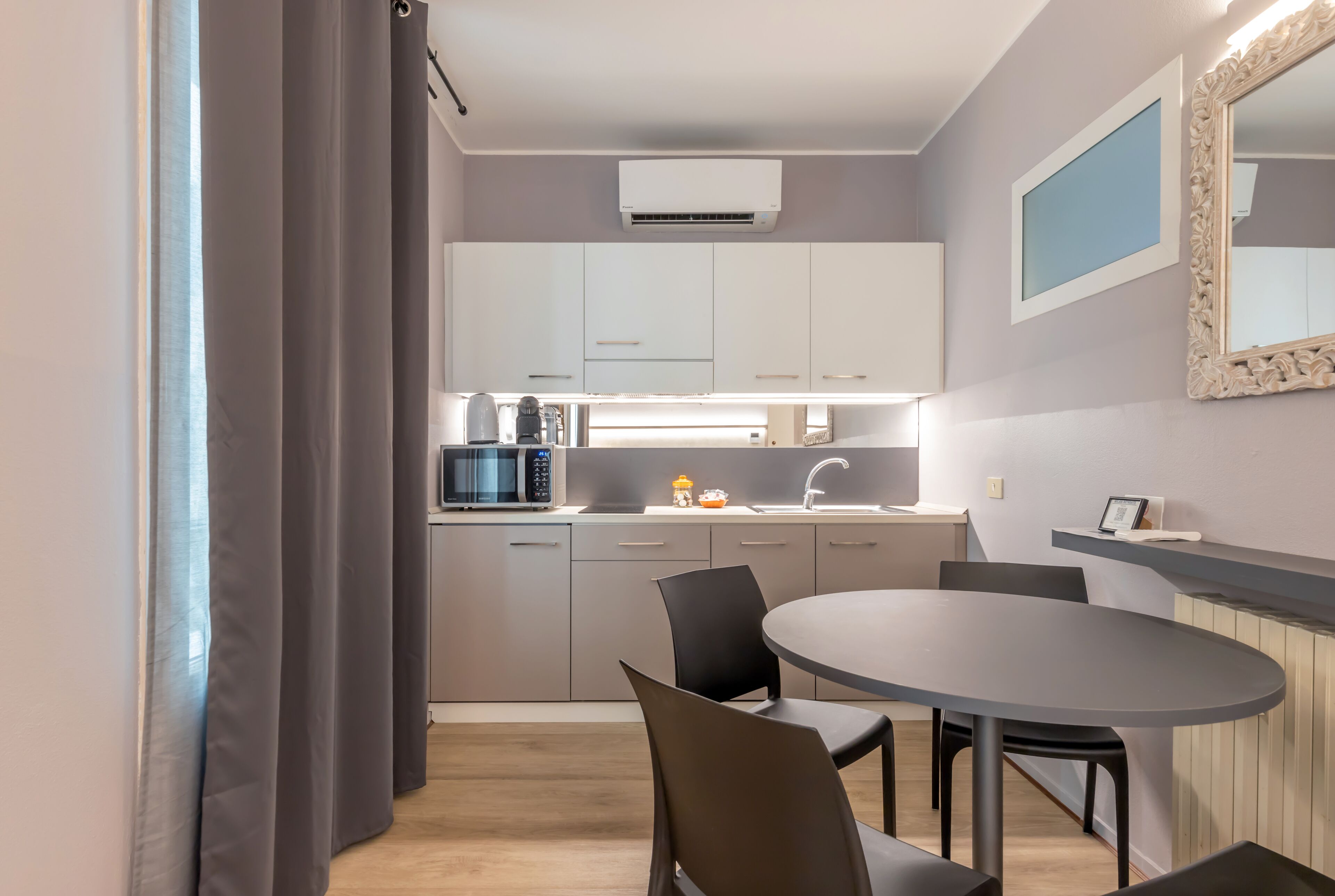 Una cocina moderna con armarios blancos, un microondas y un lavamanos. Hay una zona de comedor con una mesa redonda y sillas.