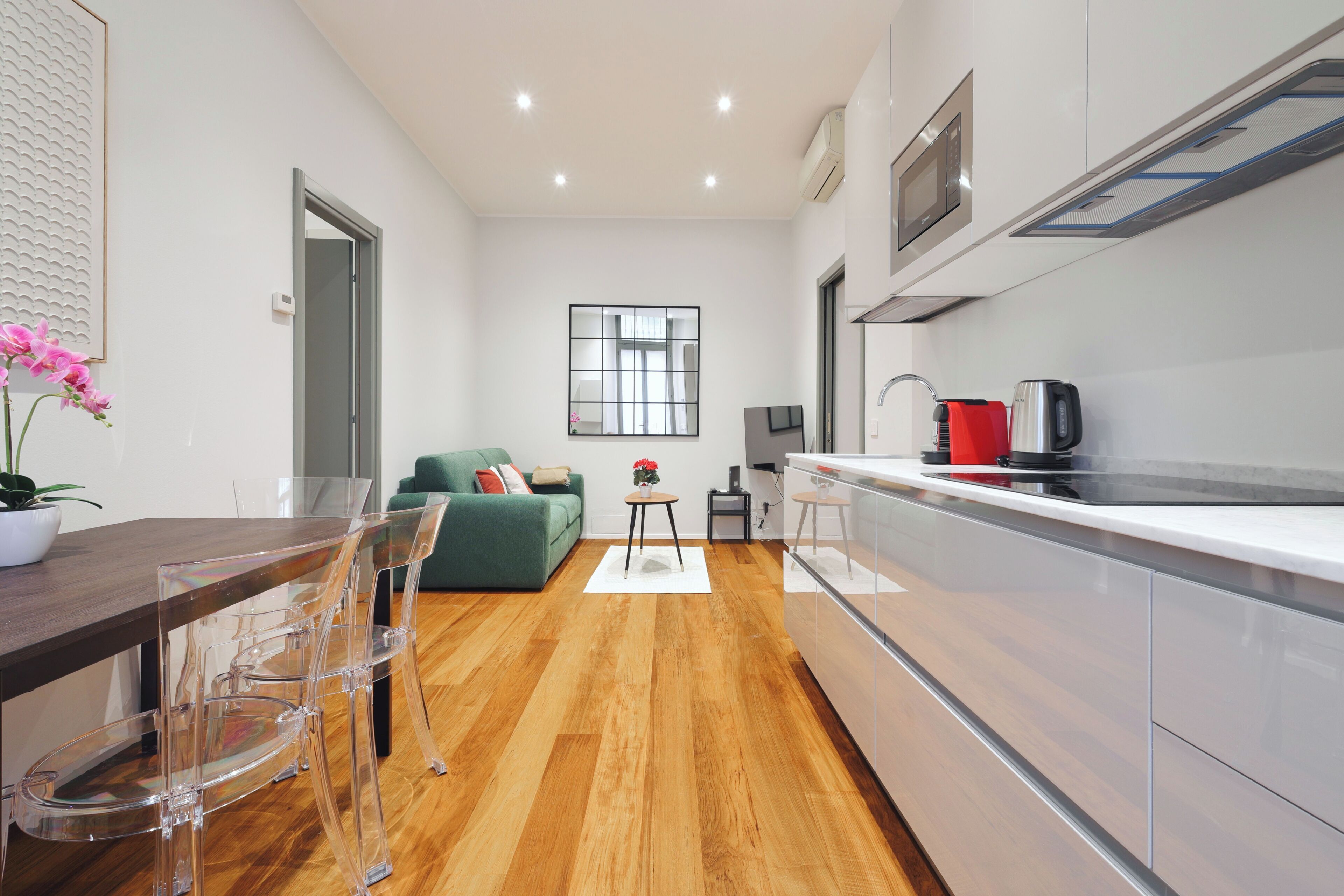 A modern kitchen with white cabinets, a wooden countertop, and a built-in oven. There is a dining area with a wooden table and clear chairs.