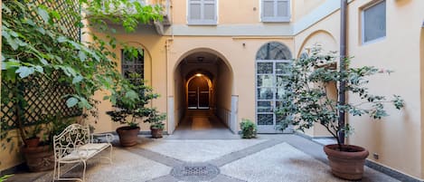 A courtyard with a bench, potted plants, and a central archway leading to a door.