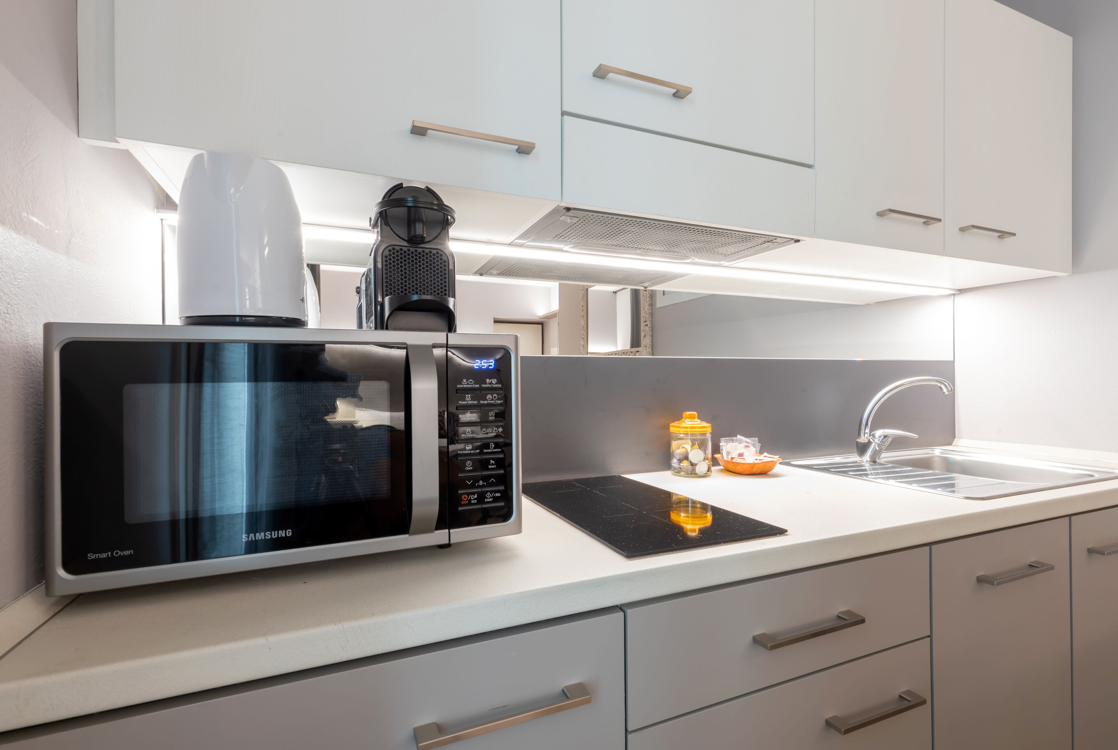 Une cuisine moderne équipée d’un four à micro-ondes encastré, d’une machine à café et d’un évier.