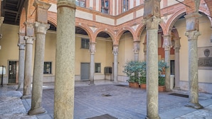 A courtyard with stone columns, arches, and potted plants. - Milan Retreats Duomo Carrobbio (Milan)
