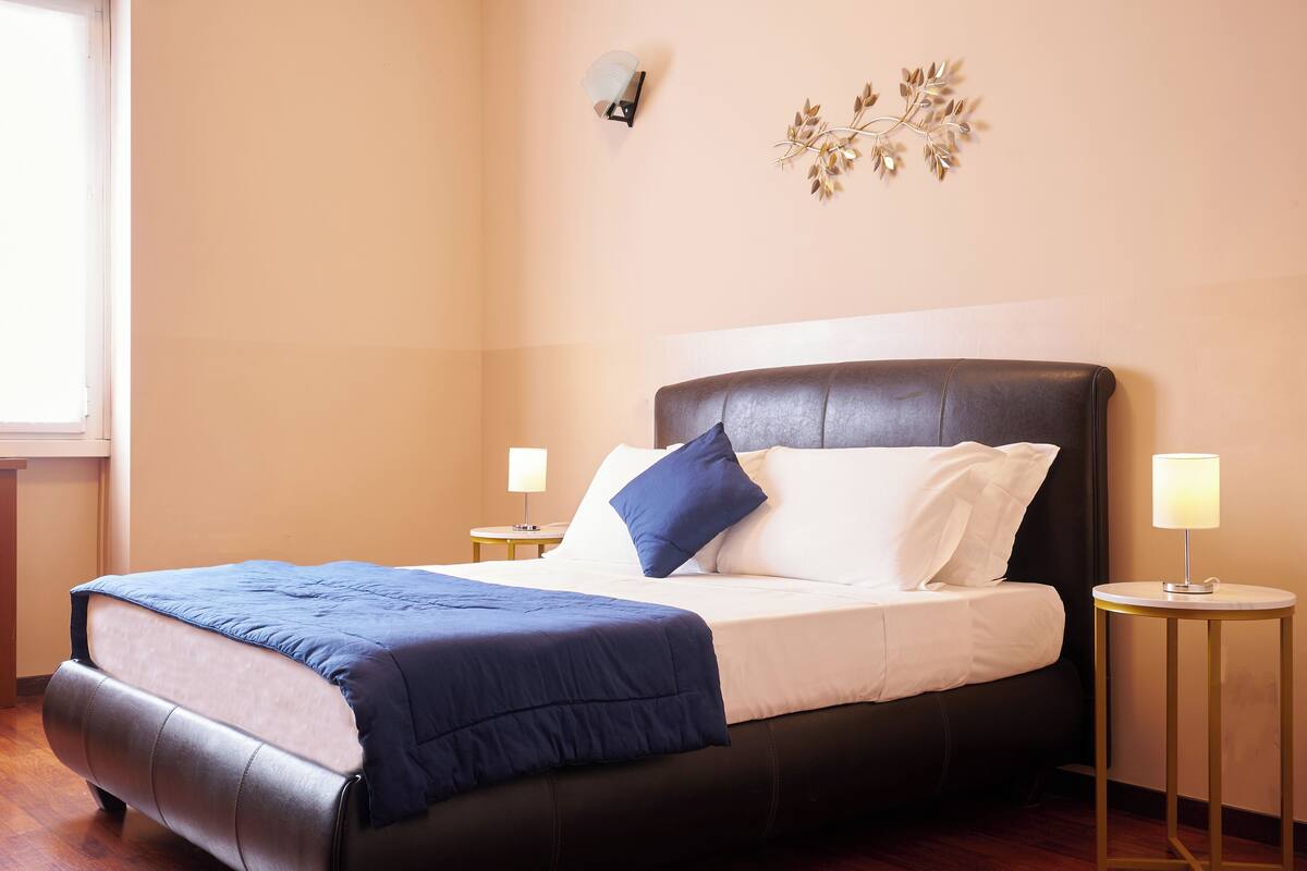A bedroom with a bed, bedside tables, and a wall-mounted light fixture.