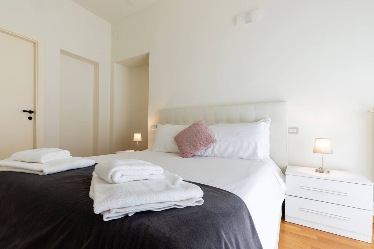 A hotel room with a bed, white nightstands, and a door.