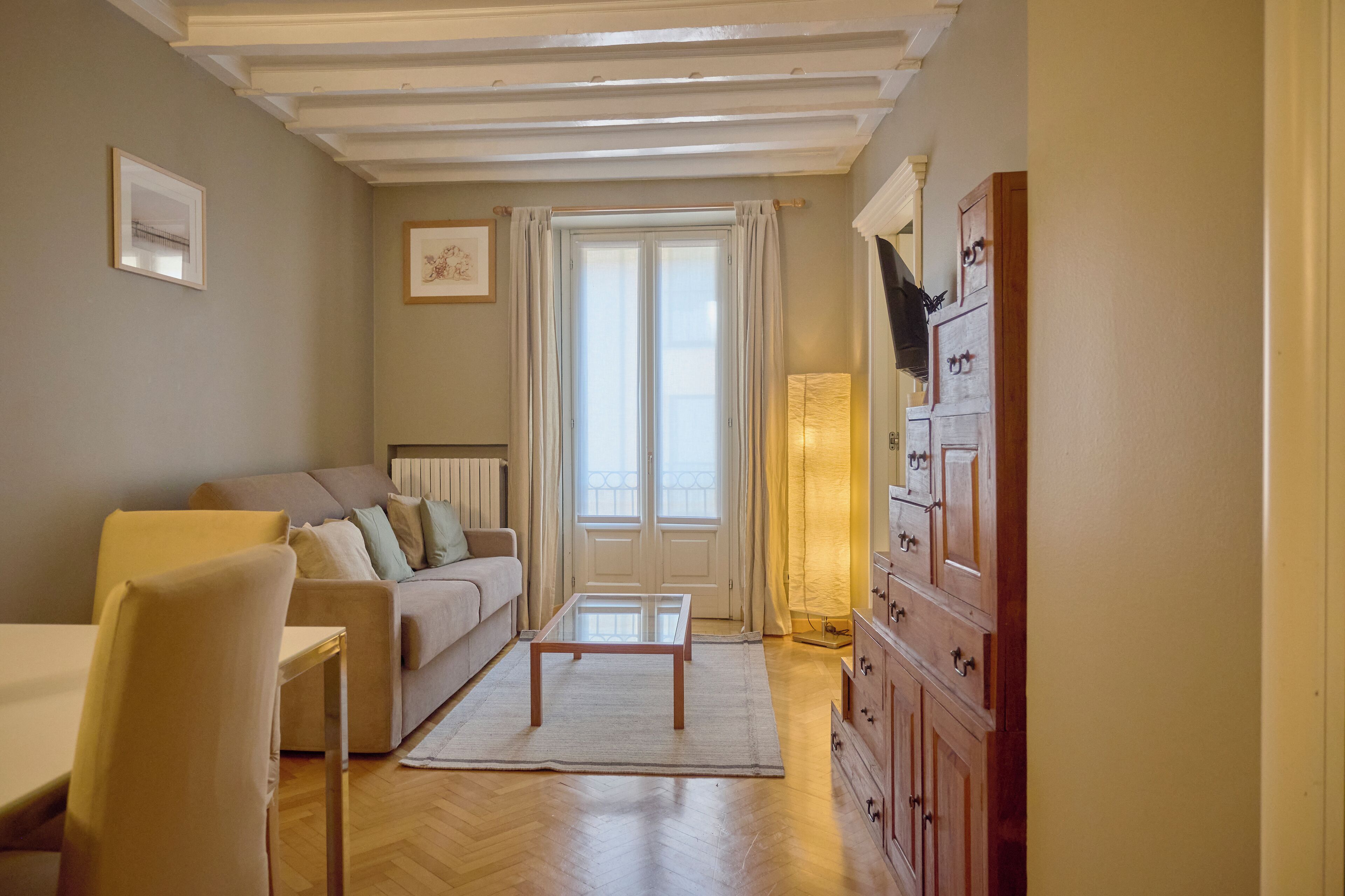 Ein Wohnzimmer mit einer Couch, einem Couchtisch, einem Holzschrank und einem Fenster mit Vorhängen.
