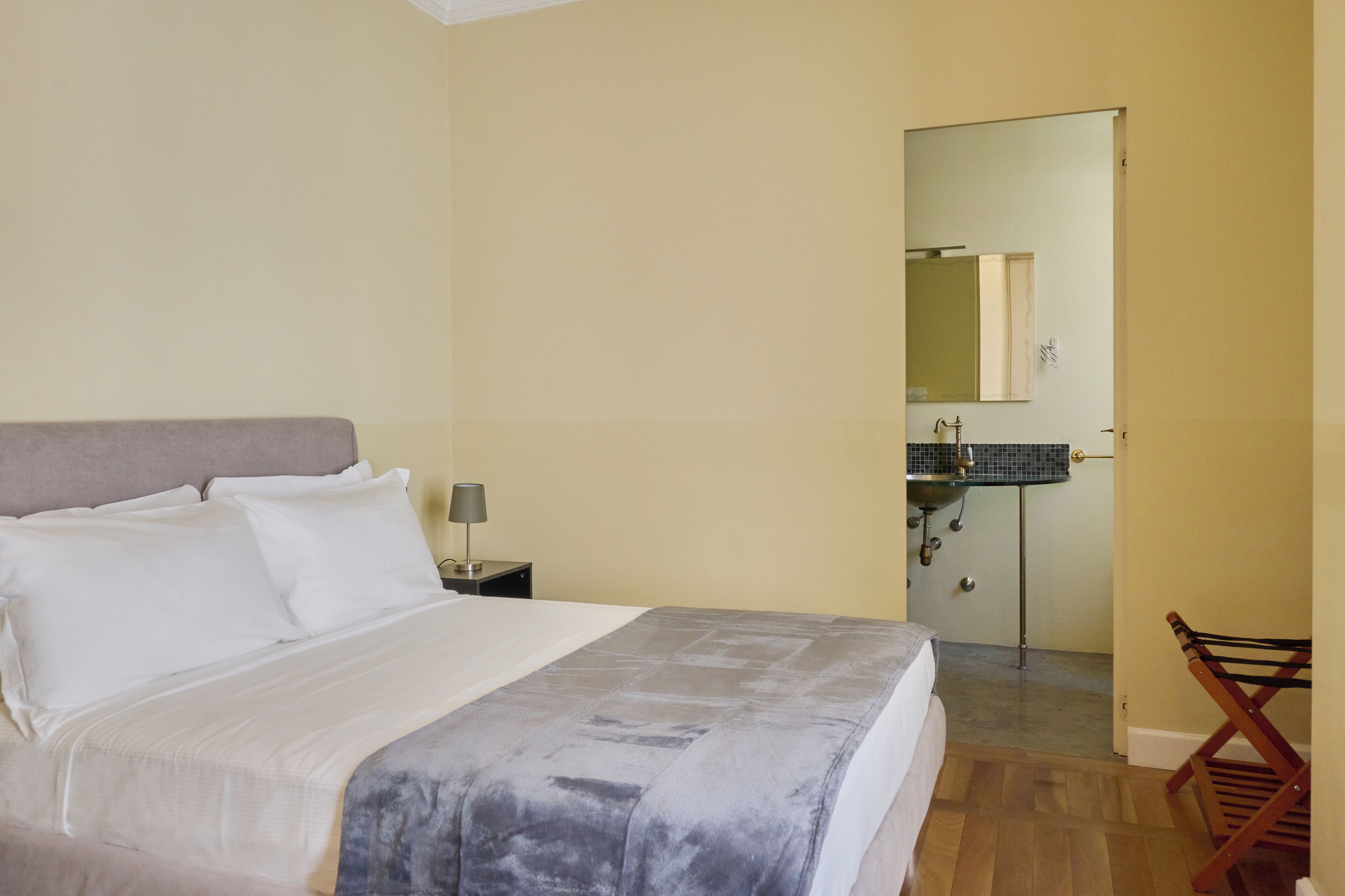 A bedroom with a bed, nightstand, lamp, and a wooden chair.