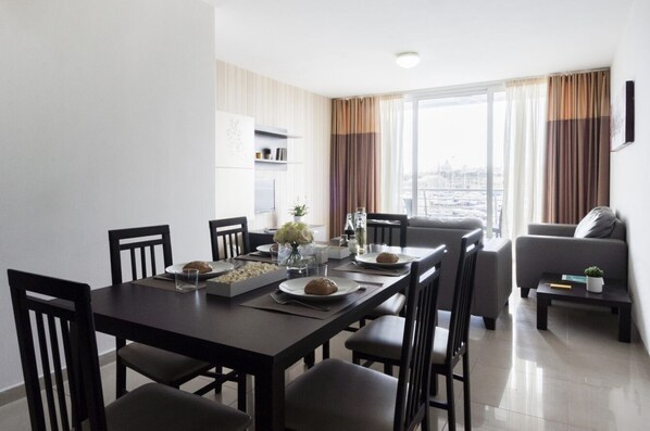 A modern dining area with a dark wooden table set for four, surrounded by chairs. A sofa and a small coffee table are visible in the background. - Valletta view Apartments by ST Hotels (Gzira)