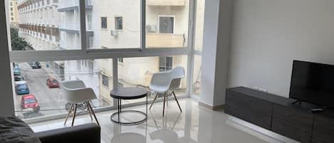 A modern living room with a large window, a sofa, two chairs, a TV, and a cabinet.