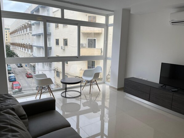 Una sala de estar moderna con un ventanal grande, un sofá, dos sillones, un televisor y un aparador.