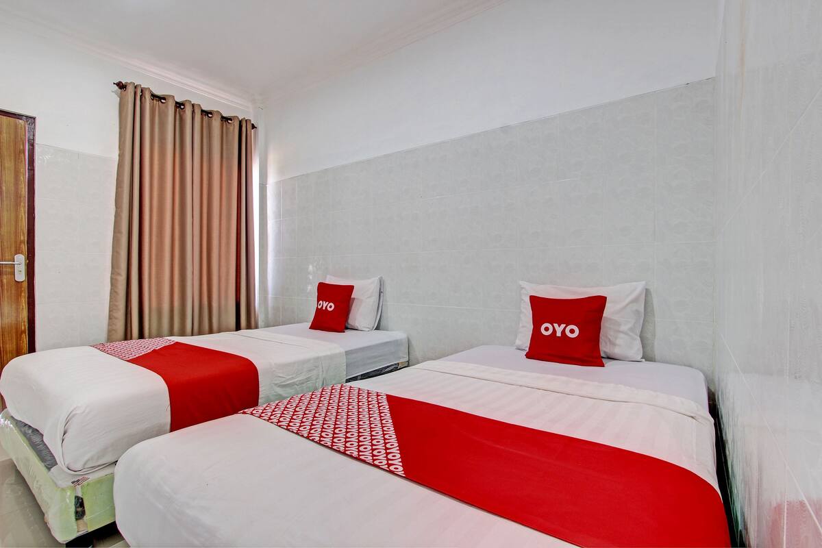A hotel room with two beds, each with a red and white bedspread, and a red pillow with the word "OYO" on it.