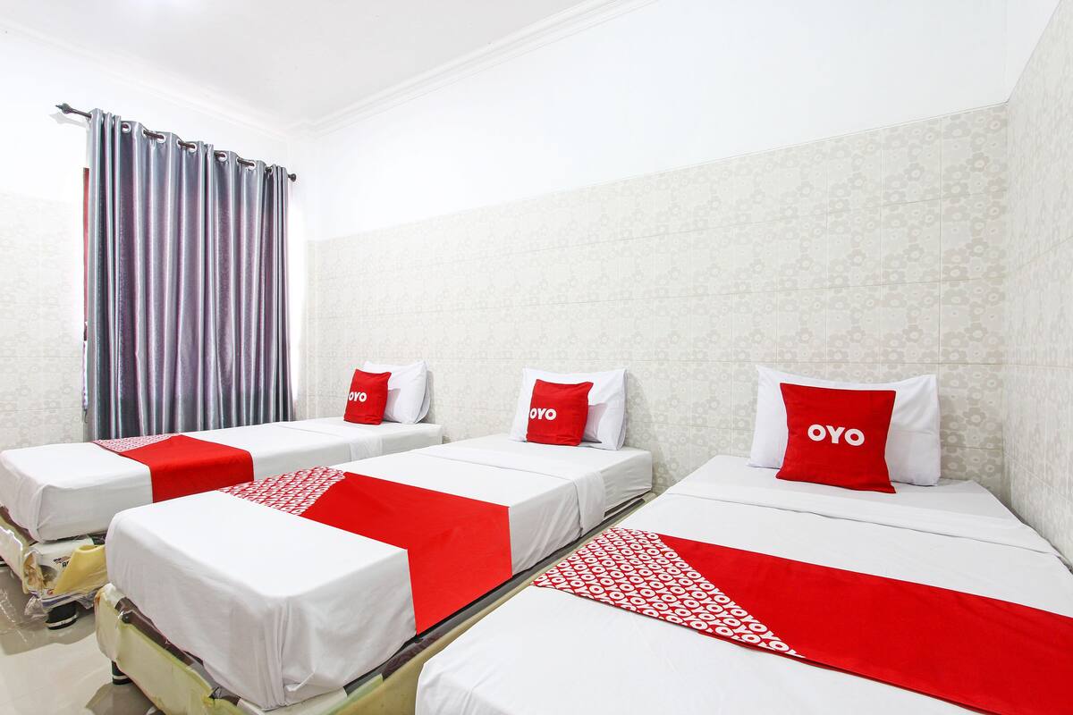 A hotel room with three single beds, each with a white and red bedspread, and matching pillows.