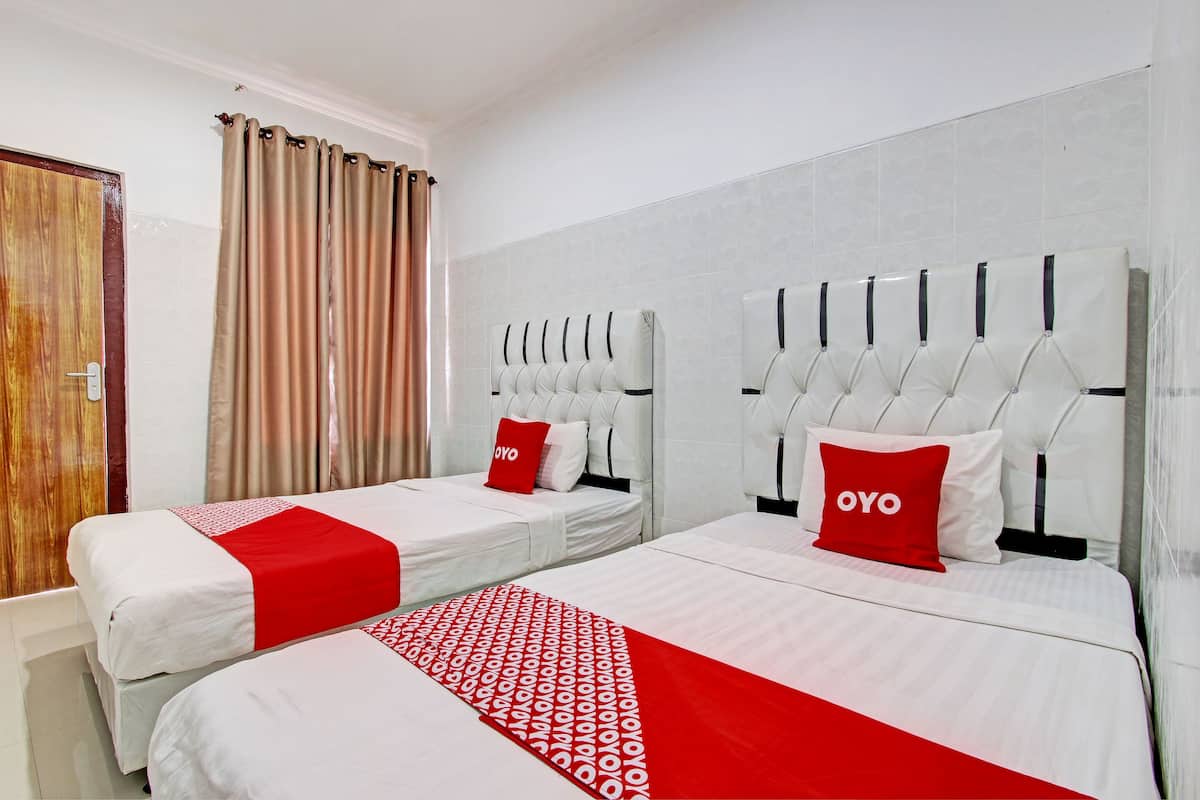 A hotel room with two beds, each with white bedding and red accents, and a large window with curtains.