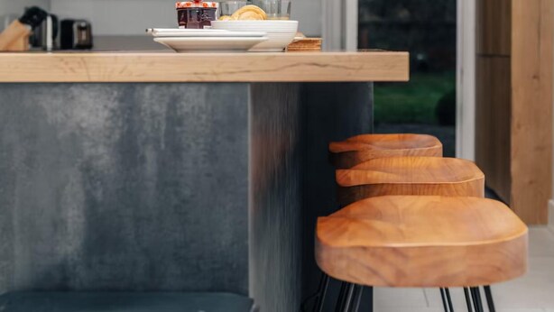 A modern kitchen with a wooden countertop, a built-in bench, and a window with a view of greenery.