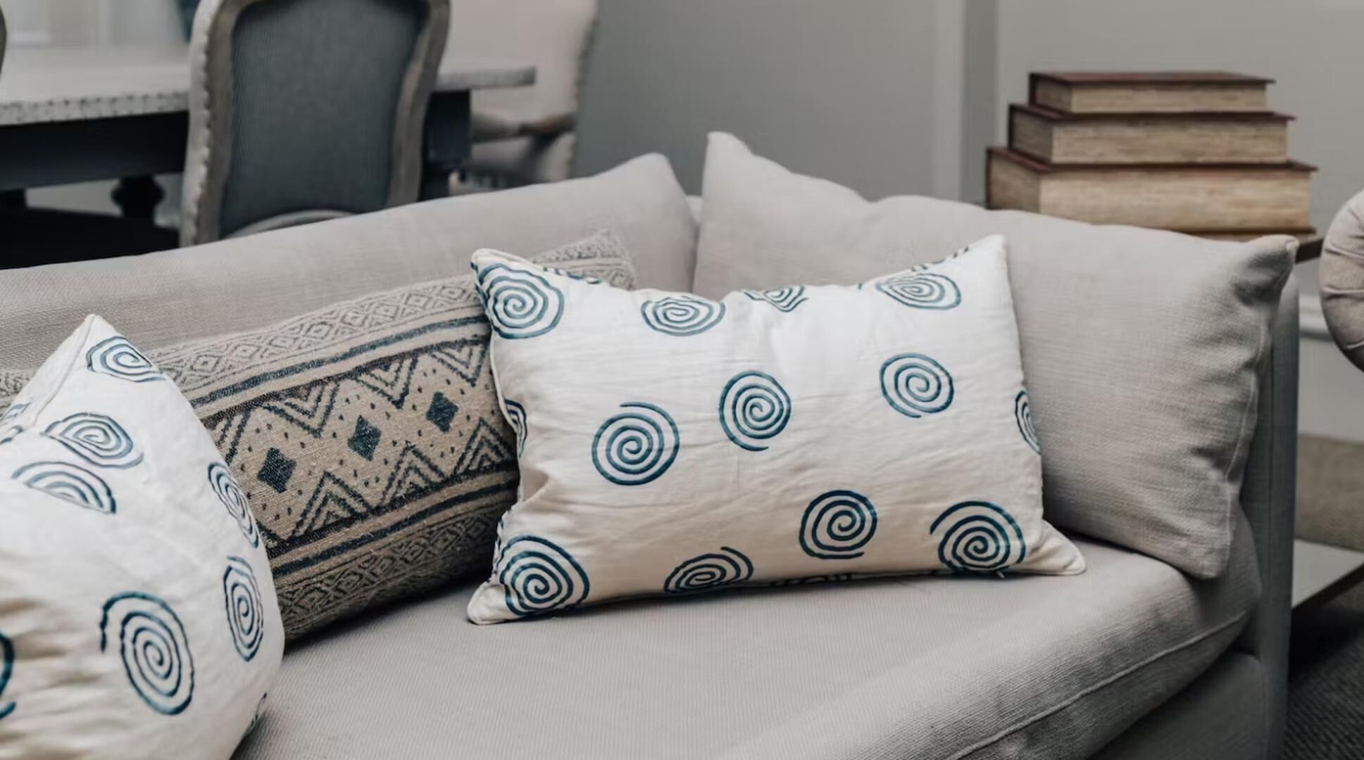 Un sofá con tres cojines decorativos, uno con un diseño geométrico y dos con motivos espirales.