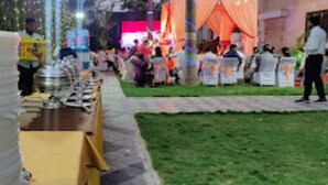 Evento al aire libre con mesas y sillas, palmeras y un edificio al fondo.