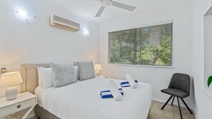 A hotel room with a bed, a chair, a window with blinds, a ceiling fan, and an air conditioning unit.